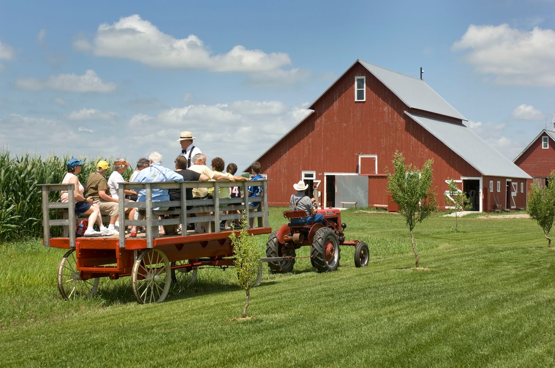 Folks on a tractor tour of Wessels Living History Farm, with a red barn and a corn field in the background.