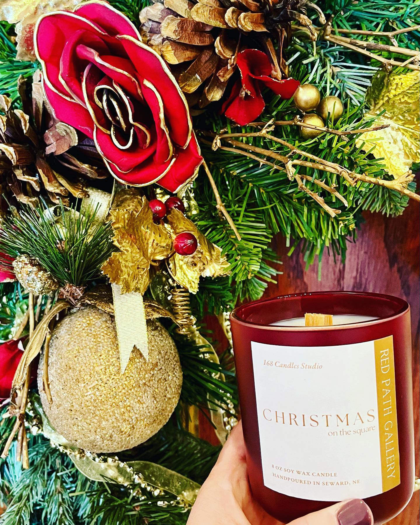 A Christmas candle in front of a Christmas tree from Red Path Gallery & Tasting Room.