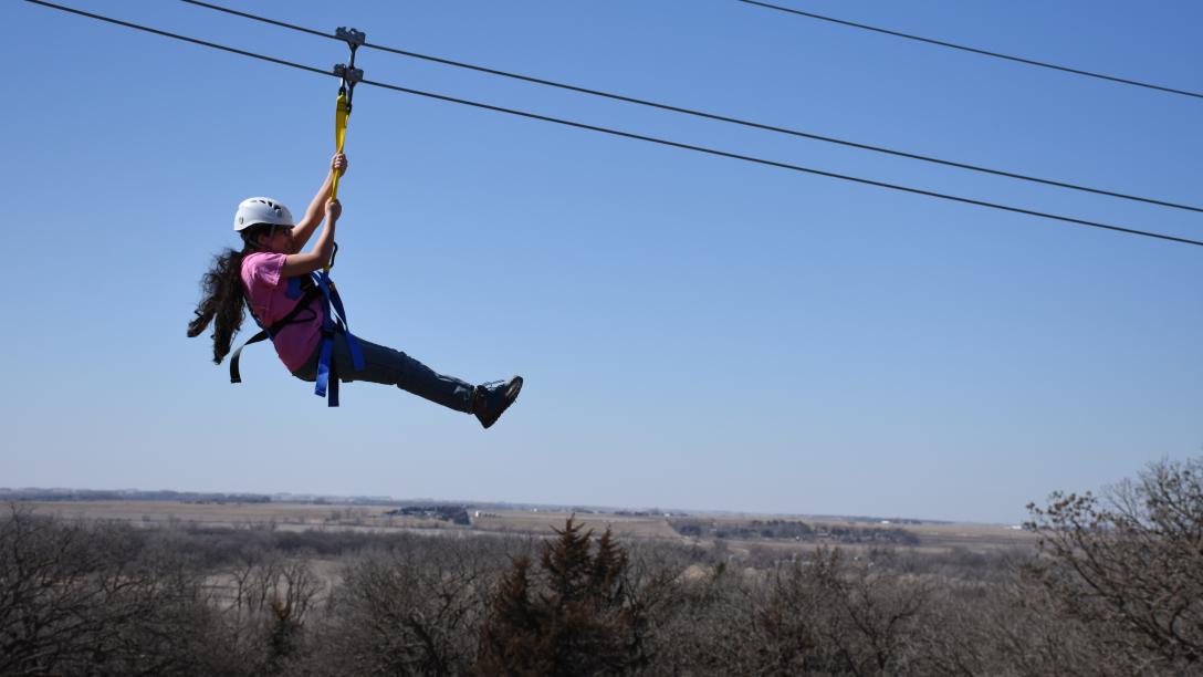 A child zip lines above the treetops on a Soaring Hawk Zip Line Tour in Nebraska.