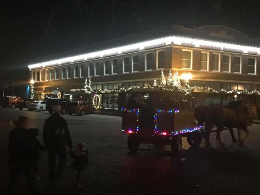 A decorated sleigh with people riding in behind a horse outside of the Shops at the Victor Anderson Building.