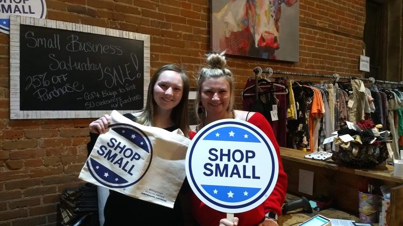 Two women hold Shop Small signs at the Mercantile Building in Beatrice