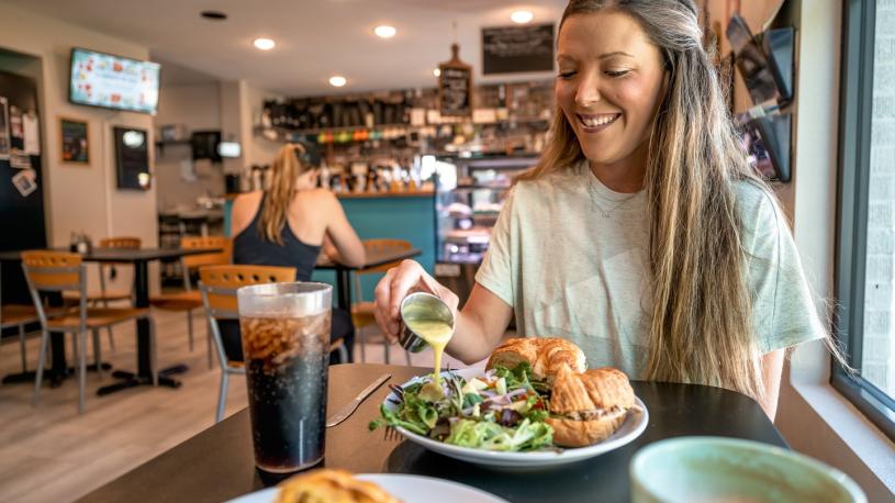 A woman pouring dressing on her salad next to a sandwich at The Mixing Bowl.