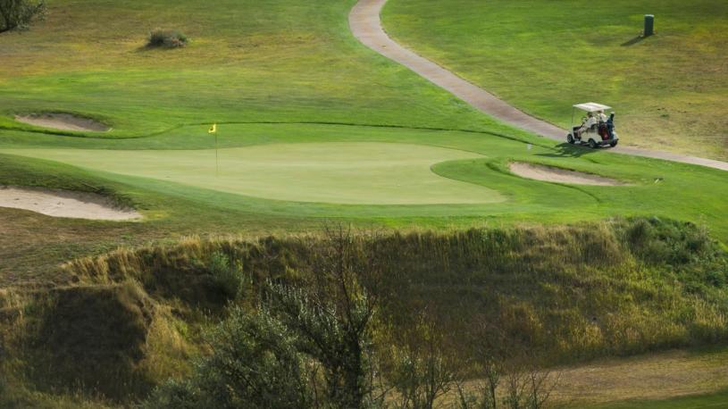 A golfcart just off the green, with a view of a hazard in the foreground at Heritage Hills Golf Course in McCook.