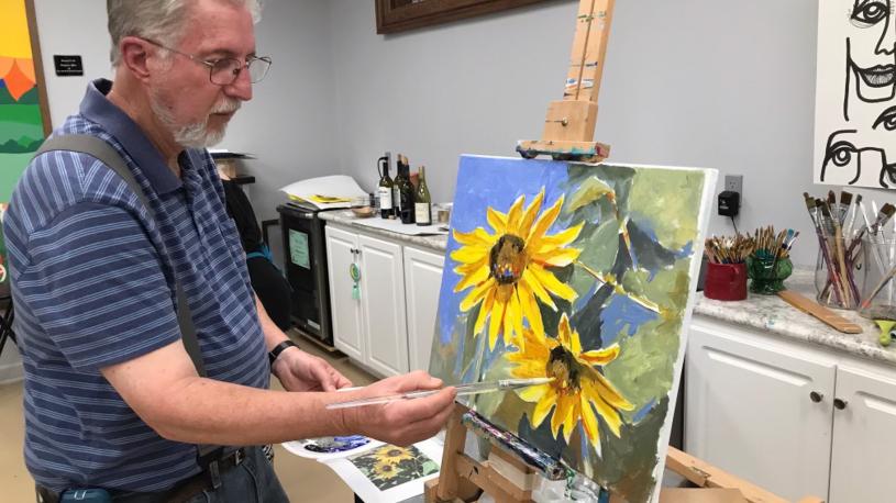 A man painting a picture of flowers at Prairie Arts Center.