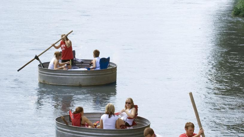 Three stock tanks floating down a Nebraska River. Folks use poles to push the tanks along the current.