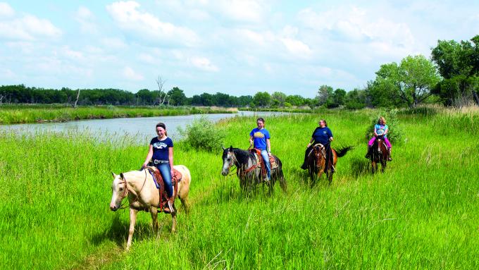 A group of kids and adults horseback riding with Dusty Trails along a river in Nebraska.